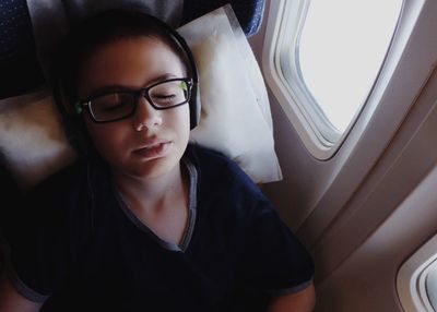 High angle view of woman with headphones sleeping by window in airplane