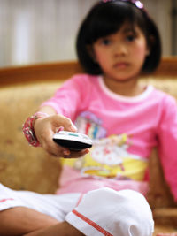 Close-up of girl holding remote control while sitting at home