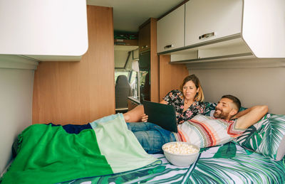 Couple watching a movie on the tablet lying on the bed of their camper van