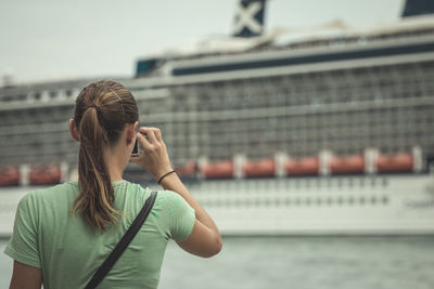 Rear view of woman photographing cruise ship