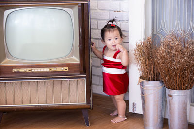Portrait of cute girl standing by vintage television at home