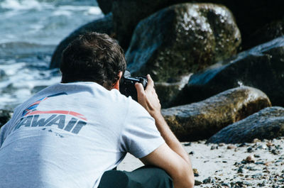 Rear view of man photographing rock on rocks