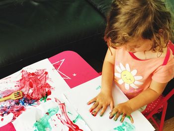 High angle view of cute girl painting on paper with hands while sitting at home