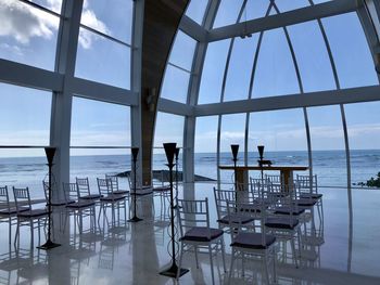 Chairs and table by sea against sky seen through glass window