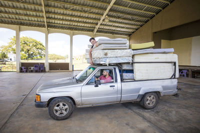 Two men riding on loaded truck help to move mattresses at orphanage.