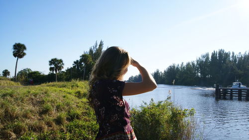 Woman shielding eyes while standing by lake on field