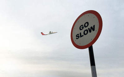 Low angle view of roadsign against airplane