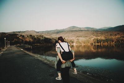 Rear view of man piggybacking woman while walking on road