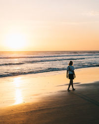 Woman walking at beach against sky during sunset