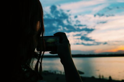 Close-up of woman photographing through smart phone against sky