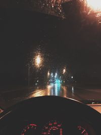 Close-up of wet car on illuminated road during rainy season