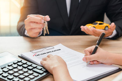 Cropped image of man signing documents with agent holding keys and toy car on table
