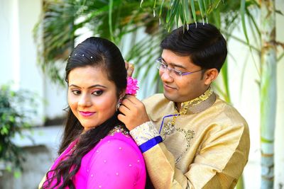 Boyfriend adjusting flower in girlfriend hair against tree 