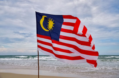 Waving malaysia national also known as jalur gemilang flag by the seashore.