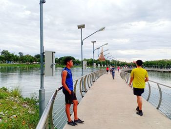 Rear view of men standing by railing against sky