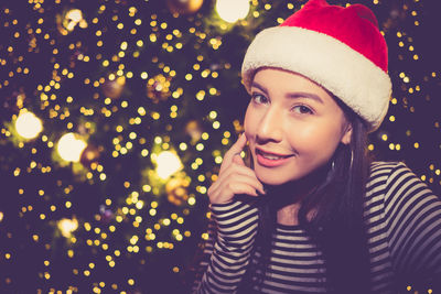 Portrait of smiling young woman against christmas tree