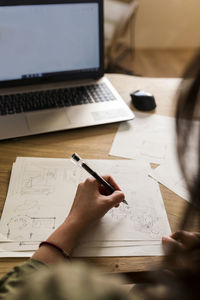 Female carpenter with laptop making design on paper at desk in industry