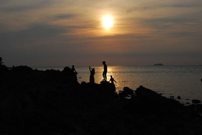 Silhouette people on beach against sky during sunset