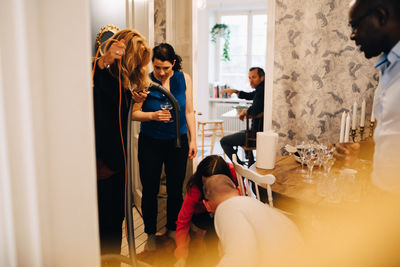 Man and woman using vacuum cleaner while friends standing by table at home