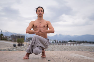 Shirtless man doing yoga on pier