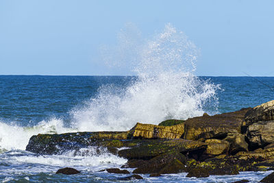 Sea waves splashing on rocks against clear sky