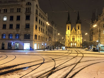 Illuminated railroad tracks by buildings in city at night