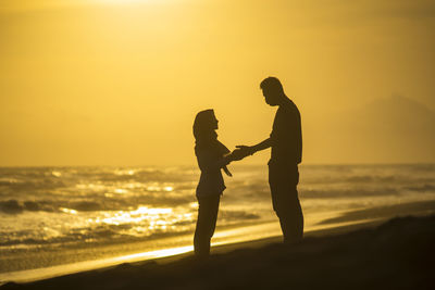 Silhouette couple standing on beach during sunset