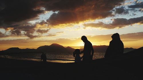 Silhouette people on beach against sky during sunset