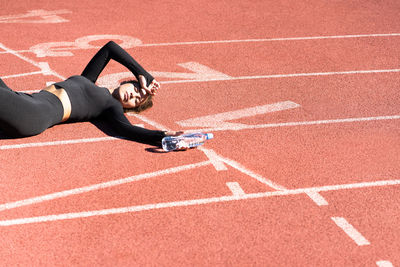 High angle view of tired woman lying with water bottle on running track