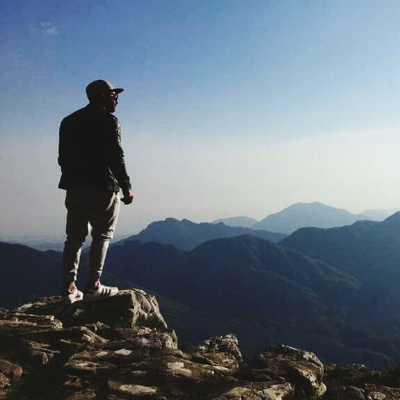 MAN STANDING ON ROCK AGAINST MOUNTAIN RANGE