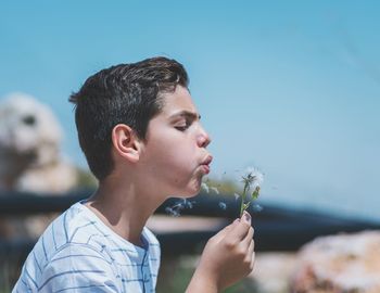 Close-up of boy blowing dandelion against sky