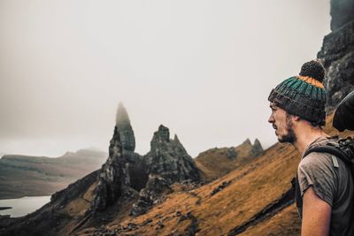 Side view of young man standing on mountain against sky