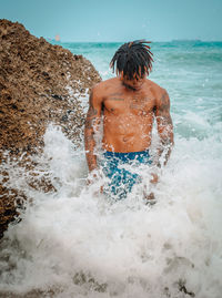 Rear view of shirtless man with tattoos splashing water in sea