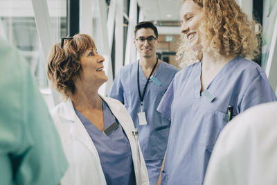 Happy female healthcare workers looking at each other standing in corridor at hospital