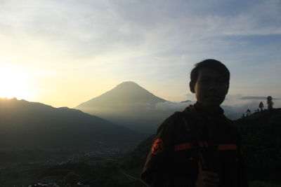 Boy standing on mountain against sky during sunset