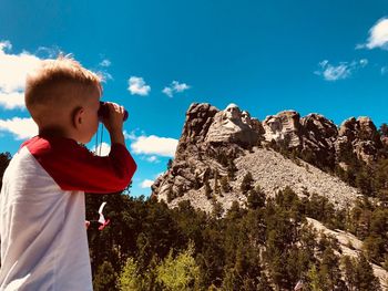Boy standing on rock formation against sky