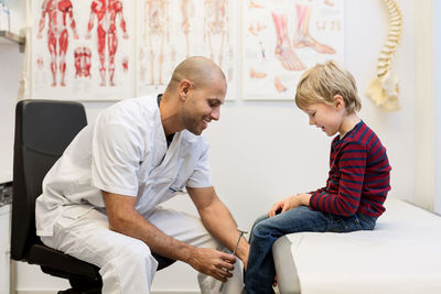 Male doctor checking knee reflexes of boy at orthopedic clinic