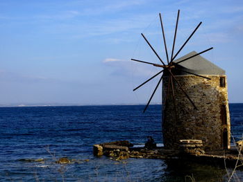 Traditional windmill by sea against sky