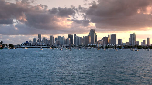 Sea by buildings against sky during sunset