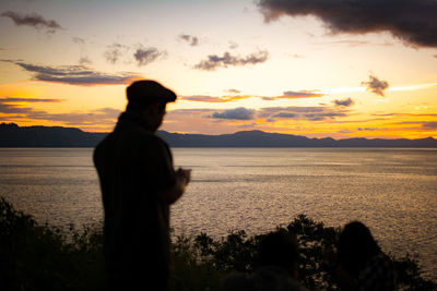 Silhouette man looking at sea against sky during sunset