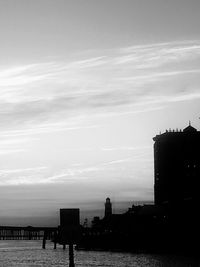 Silhouette buildings by sea against sky at sunset