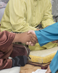 Cropped image of people shaking hands with man sitting in background