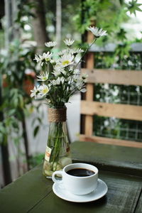 Close-up of coffee by white flower vase on table