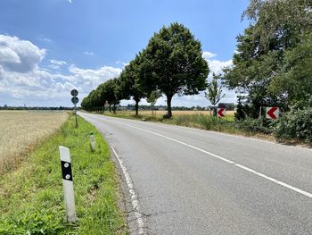 Road by trees on field against sky