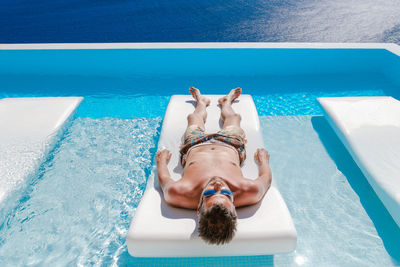 High angle view of young man lying on lounge chair in swimming pool