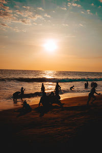 Silhouette people on beach against sky during sunset