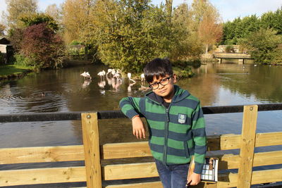 Portrait of boy leaning on railing while standing against flamingos in pond