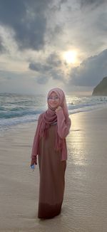 Woman standing at beach against sky during sunset