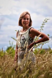 Portrait of smiling young woman standing on field against sky