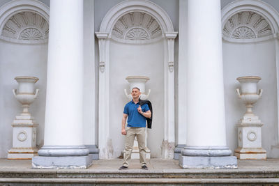 A man in casual clothes stands near the columns of a white building person